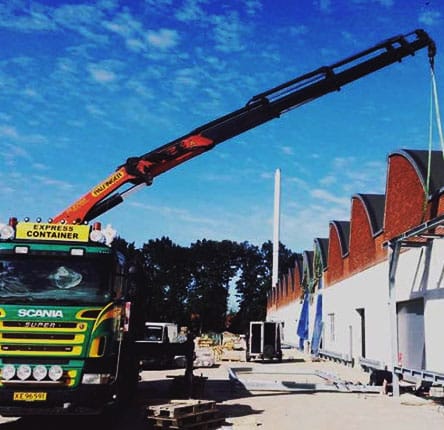 Grøn og gul farvet lastbil med en rød kran i byggelandskab med letskyet blå himmel